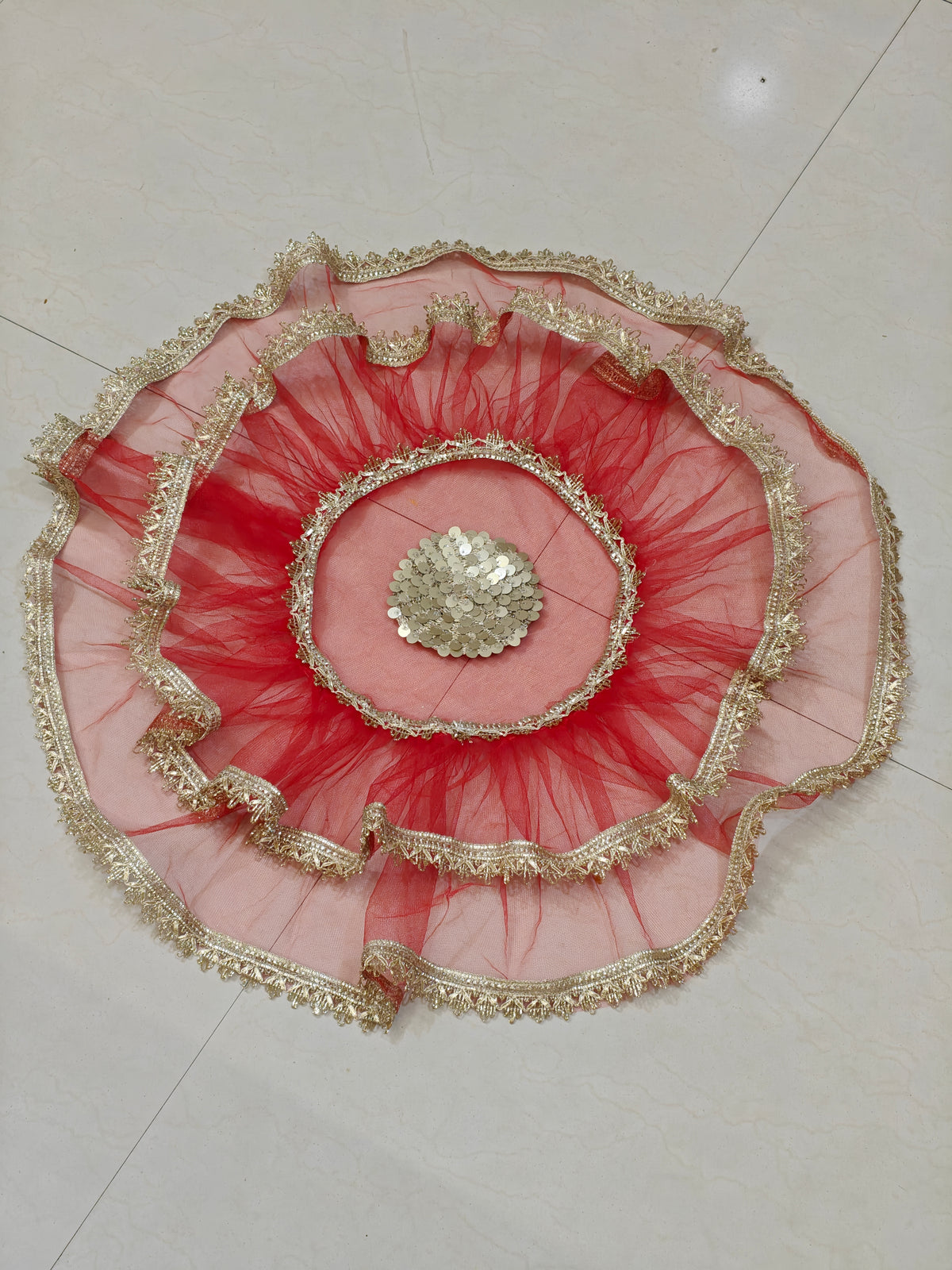 Red net thaal cover with layered ruffles, golden lace border and decorative sequin centre, 25 inches diameter.