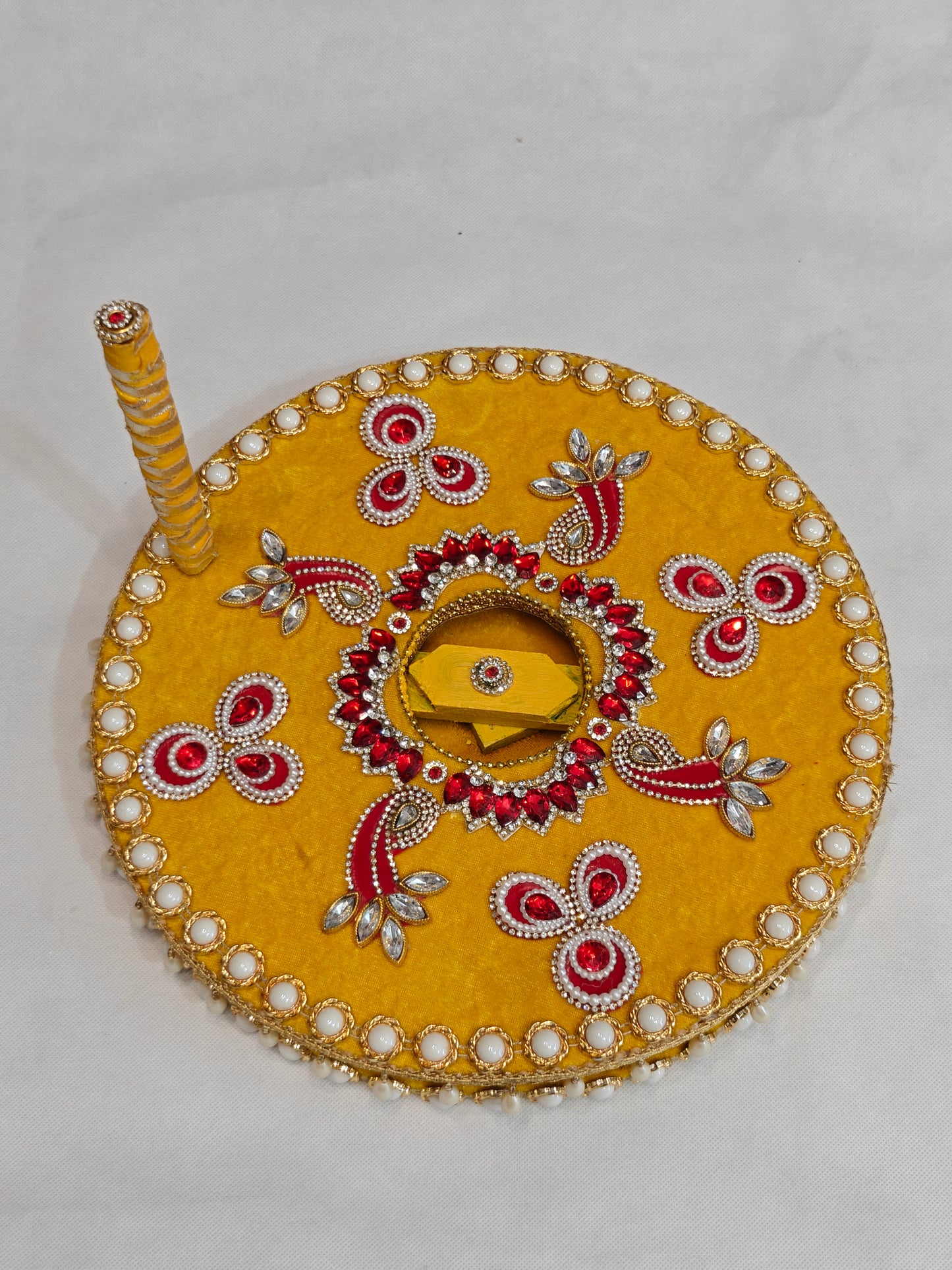 Top view of handcrafted yellow velvet decorative chakki for Baan ceremony showing intricate red kundan floral burst centre, marquise crystal leafwork, paisley motifs and white pearl cabochon border on 12 inch MDF grinding wheel