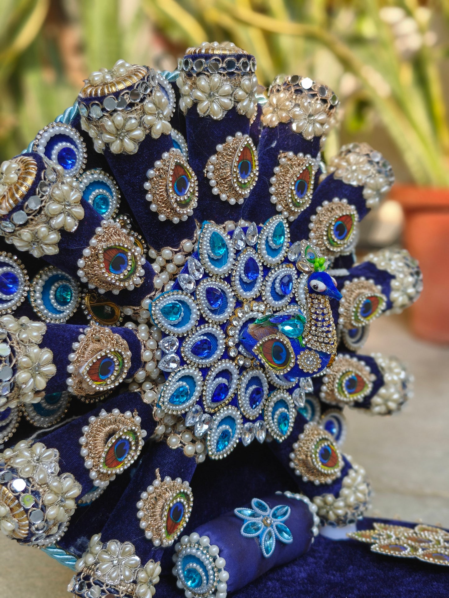 Close-up of handcrafted peacock singhasan backrest with real feather motifs, blue crystals, pearl detailing and zardozi embroidery on royal blue velvet
