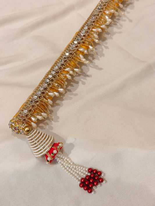 Close-up of yellow sarkanda end with white beaded cone, red and white pearl tassel and miniature jhumki charm