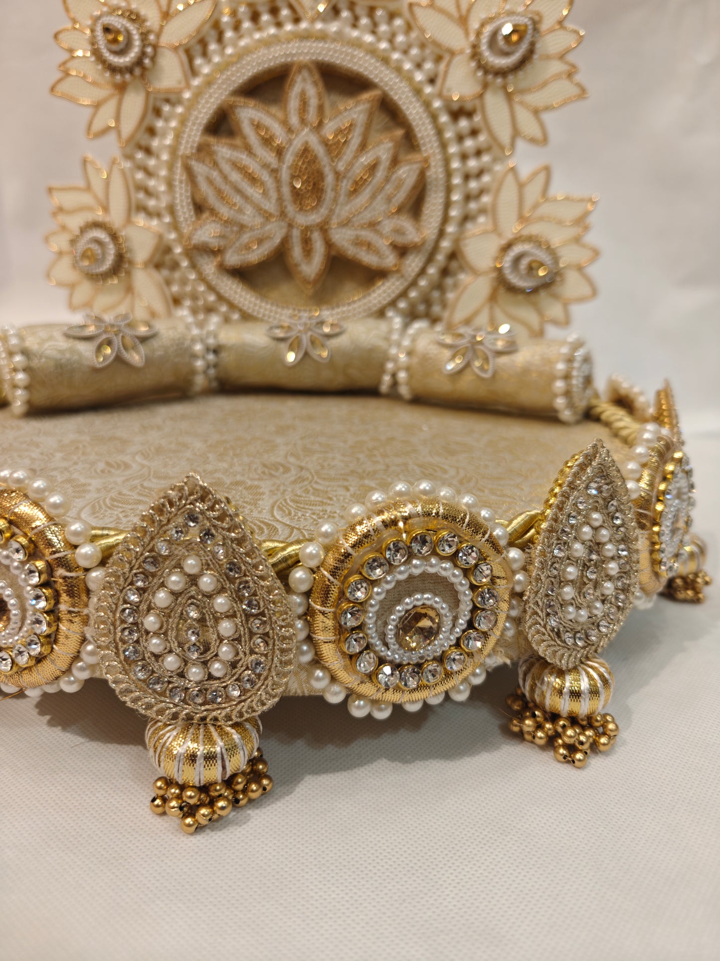 Detail view of ivory lotus garden Singhaasan base border — rhinestone teardrop and circle medallions with pearl beading, gold ghungroo tassels and brocade bolster cushions by The Wedding Station