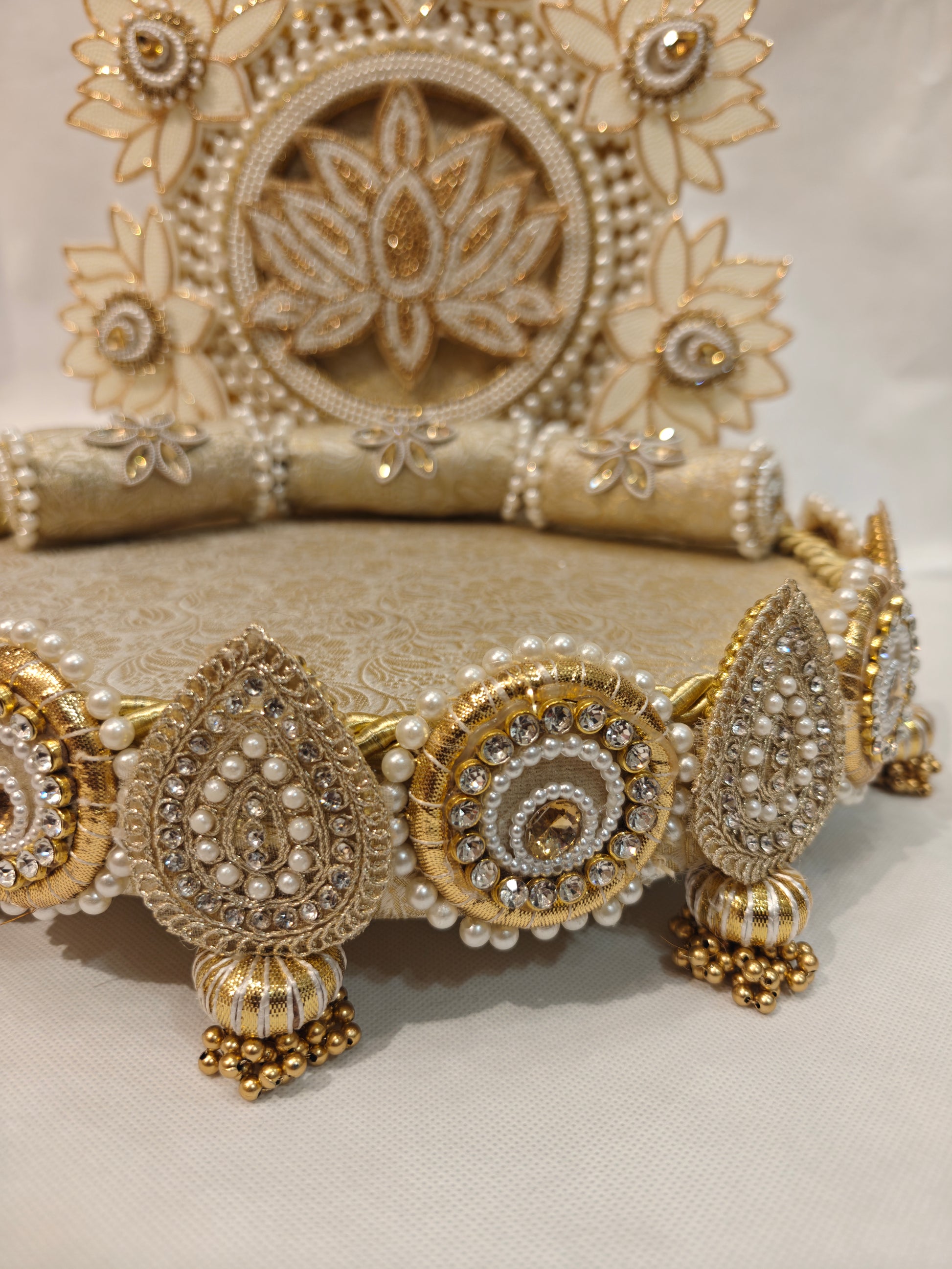 Detail view of ivory lotus garden Singhaasan base border — rhinestone teardrop and circle medallions with pearl beading, gold ghungroo tassels and brocade bolster cushions by The Wedding Station