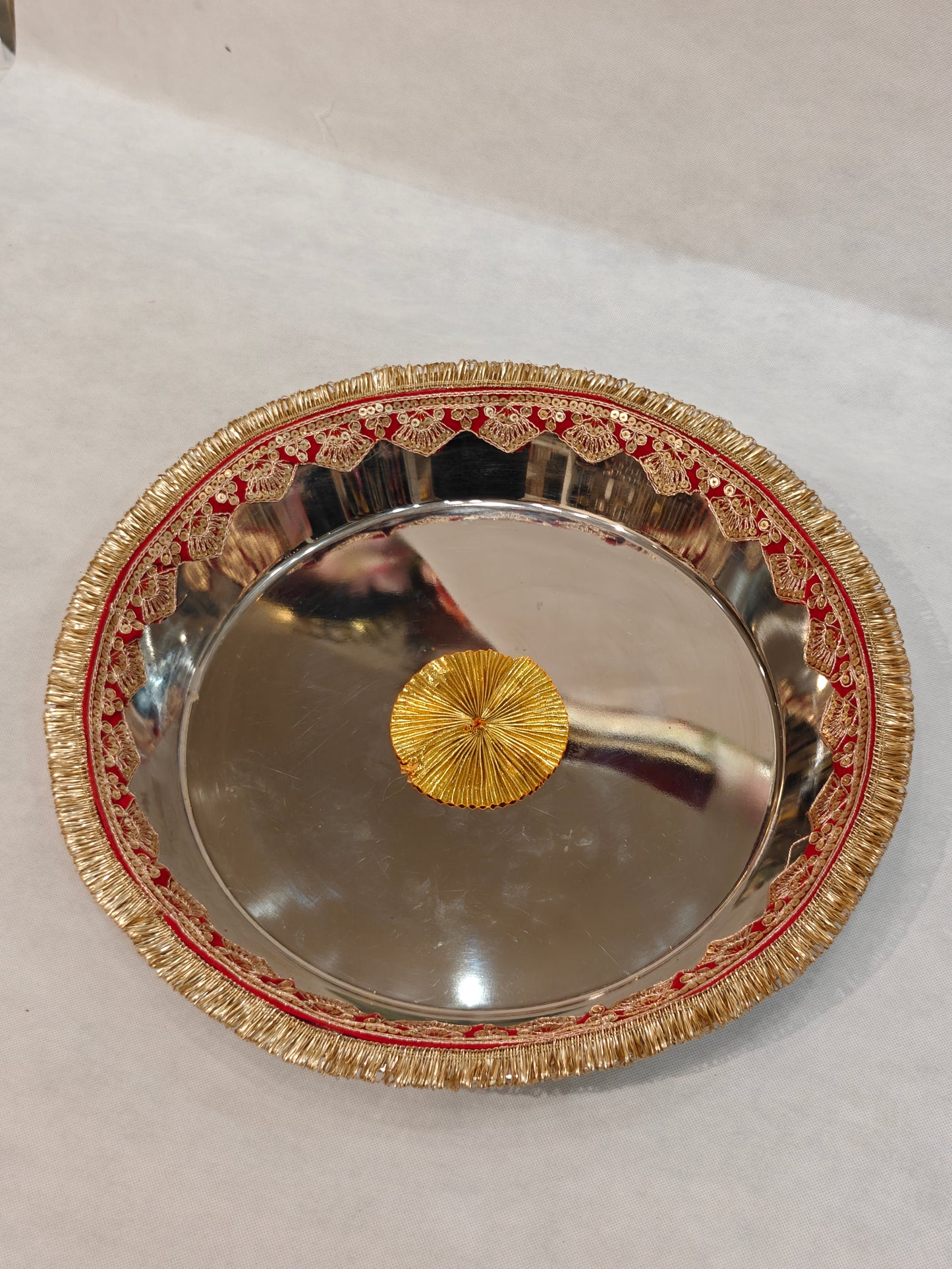 Large mirror-finish steel Pag Dhulai Thali with red velvet border, gold sequin scalloped lace, zari fringe and gold zardozi centre medallion for Indian bride's Griha Pravesh ritual