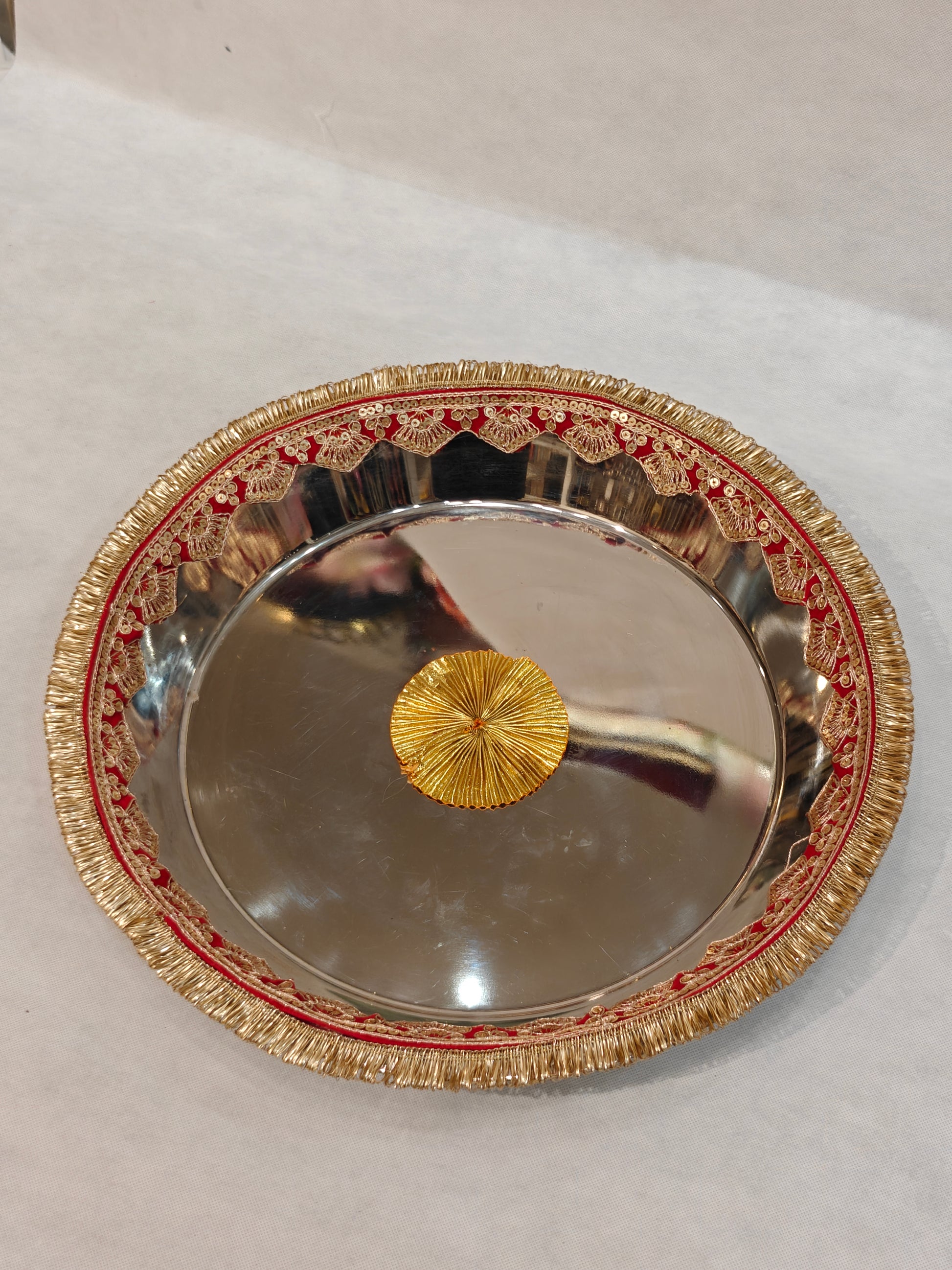Large mirror-finish steel Pag Dhulai Thali with red velvet border, gold sequin scalloped lace, zari fringe and gold zardozi centre medallion for Indian bride's Griha Pravesh ritual