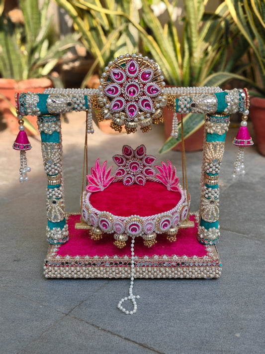 Royal Collection 2-in-1 handcrafted Ladoo Gopal jhula and singhasan in rani pink and teal velvet – decorative torana crown with fuchsia teardrop stones, teal pillar frame with mirror work and pearl clusters, detachable lotus patra singhasan with gold ghungroo fringe, MDF base with mirror border and pearl edging – The Wedding Station