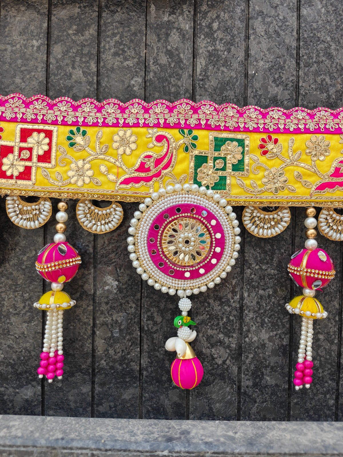 "Yellow and pink gota patti bandhanwar close-up with mirror work jhumki and hand-painted parrot pendant"