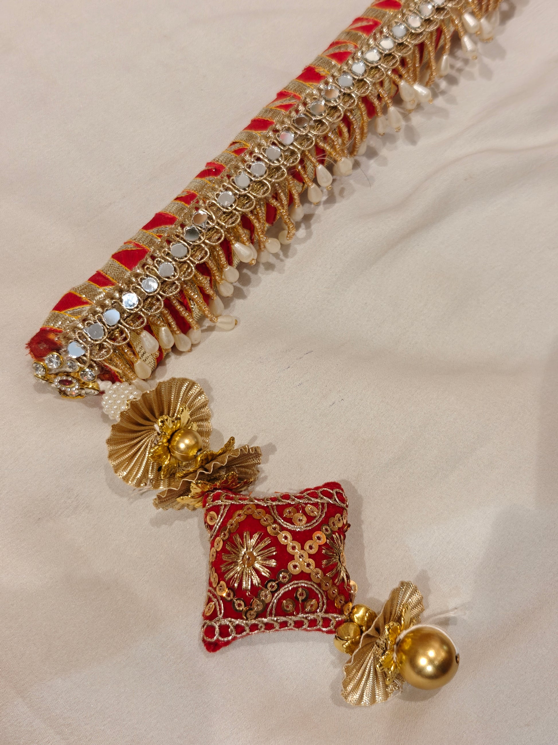 Close-up of red velvet sarkanda end with zardozi embroidered cushion, gold ghungroo, pearl drops and mirror gota-patti detailing