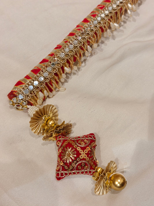 Close-up of red velvet sarkanda end with zardozi embroidered cushion, gold ghungroo, pearl drops and mirror gota-patti detailing