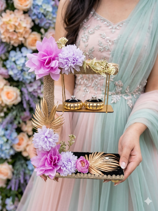 2-tier handcrafted wooden ring ceremony stand with lavender and lilac silk flowers, gold palm leaves, jute-wrapped column, swing shelf, and two gold ring holders — by The Wedding Station