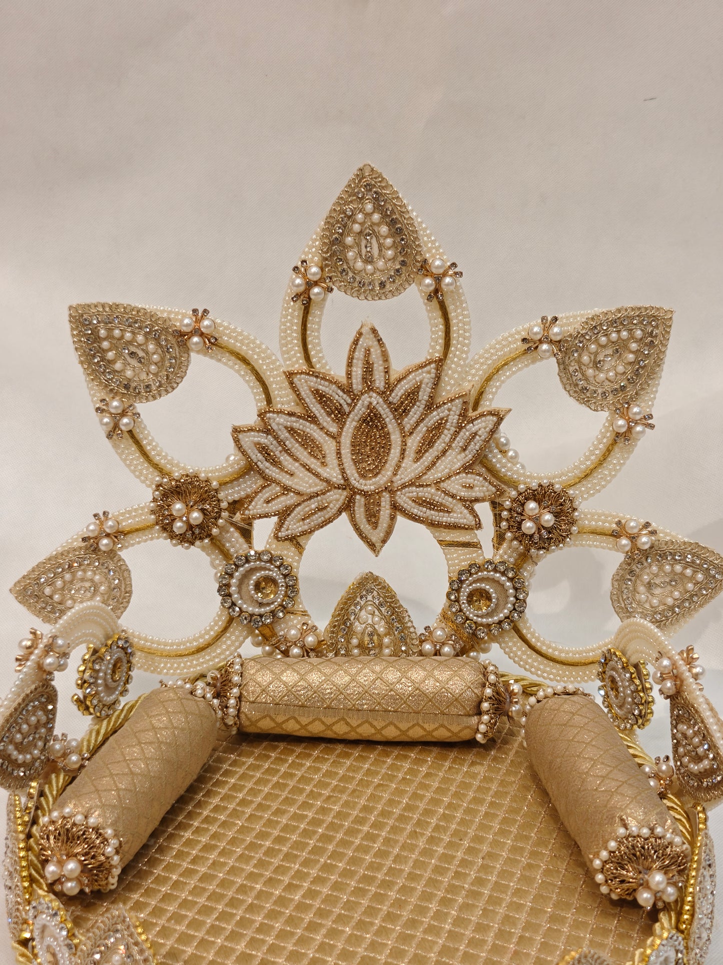 Close-up of gold lotus Singhaasan backdrop for Ladoo Gopal — ivory pearl beaded open-fret lotus crown, rhinestone medallions, gold quilted seating and bolster cushions by The Wedding Station