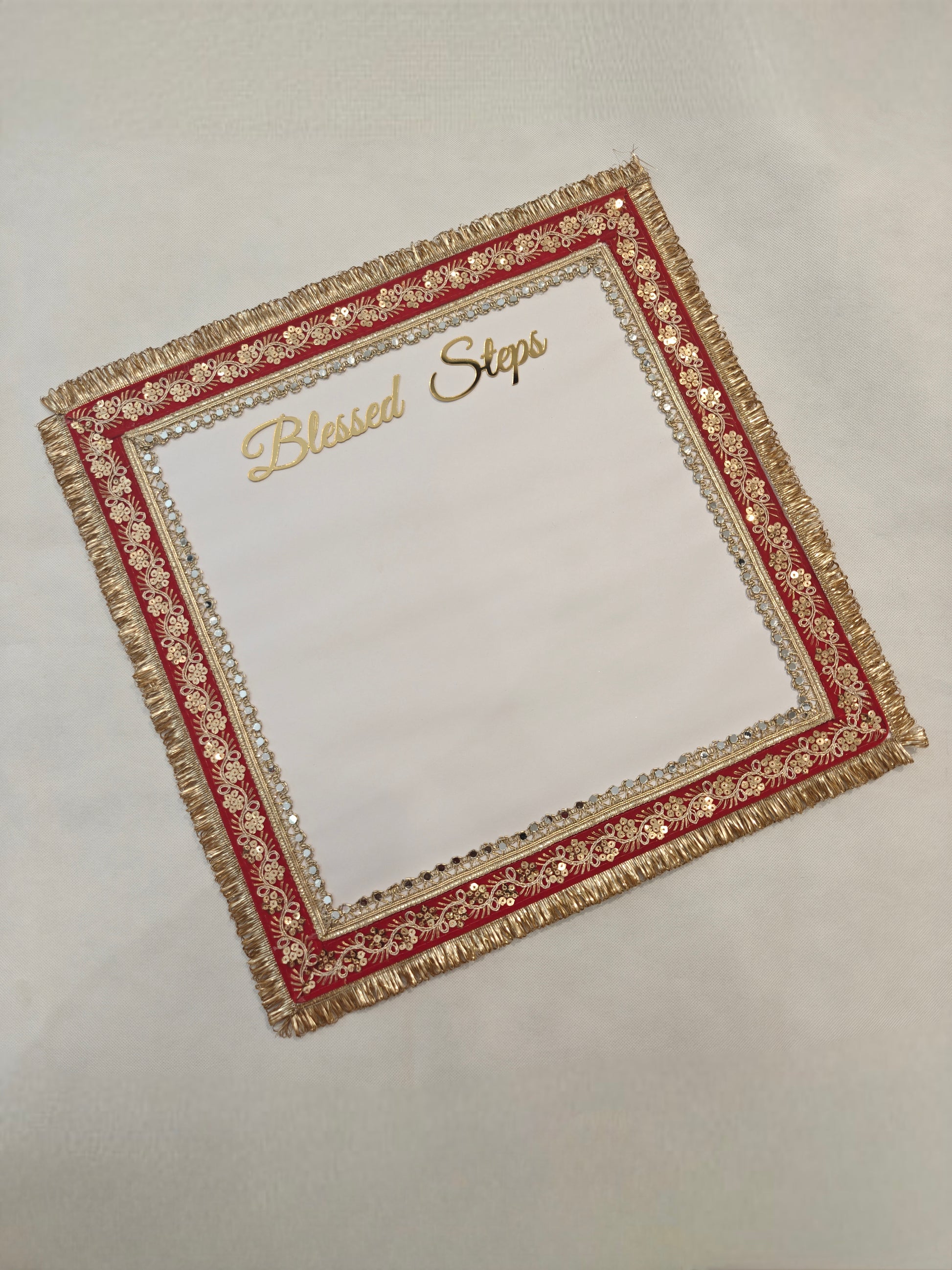 Handcrafted square white footprint mat with gold acrylic "Blessed Steps" script, outer gold zari fringe, red fabric border with gold sequin floral embroidery and inner crystal rhinestone trim on MDF base — Griha Pravesh and shop opening ceremony mat by The Wedding Station Meerut