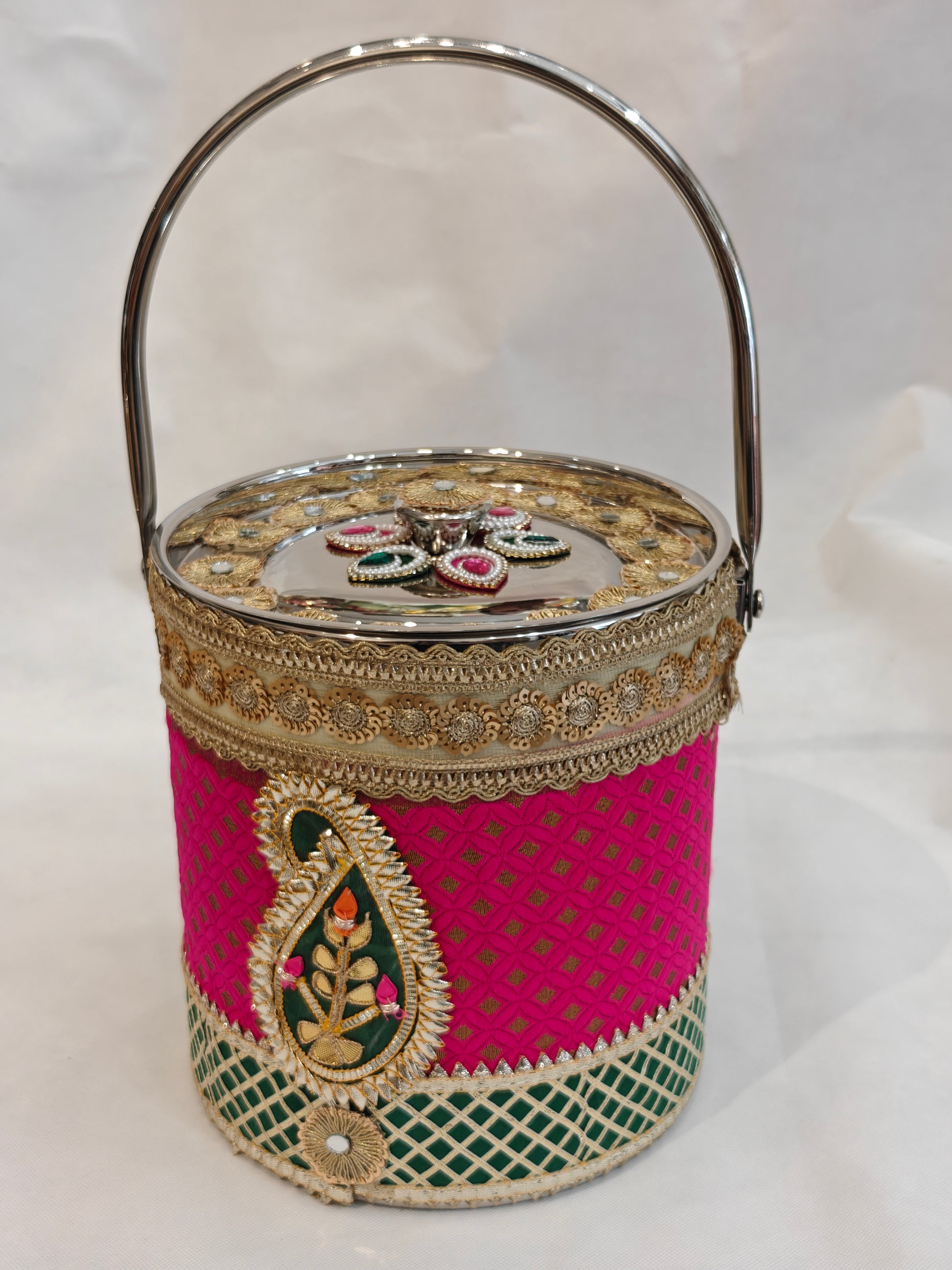 Decorated stainless steel bucket with arched handle for Indian wedding trousseau in hot pink and green brocade with gold diamond lattice, kundan paisley appliqué, gold zari scalloped lace and mirror-finish lid with gold zardozi sunflower medallions — 8.25 inch diameter, 9 inch height