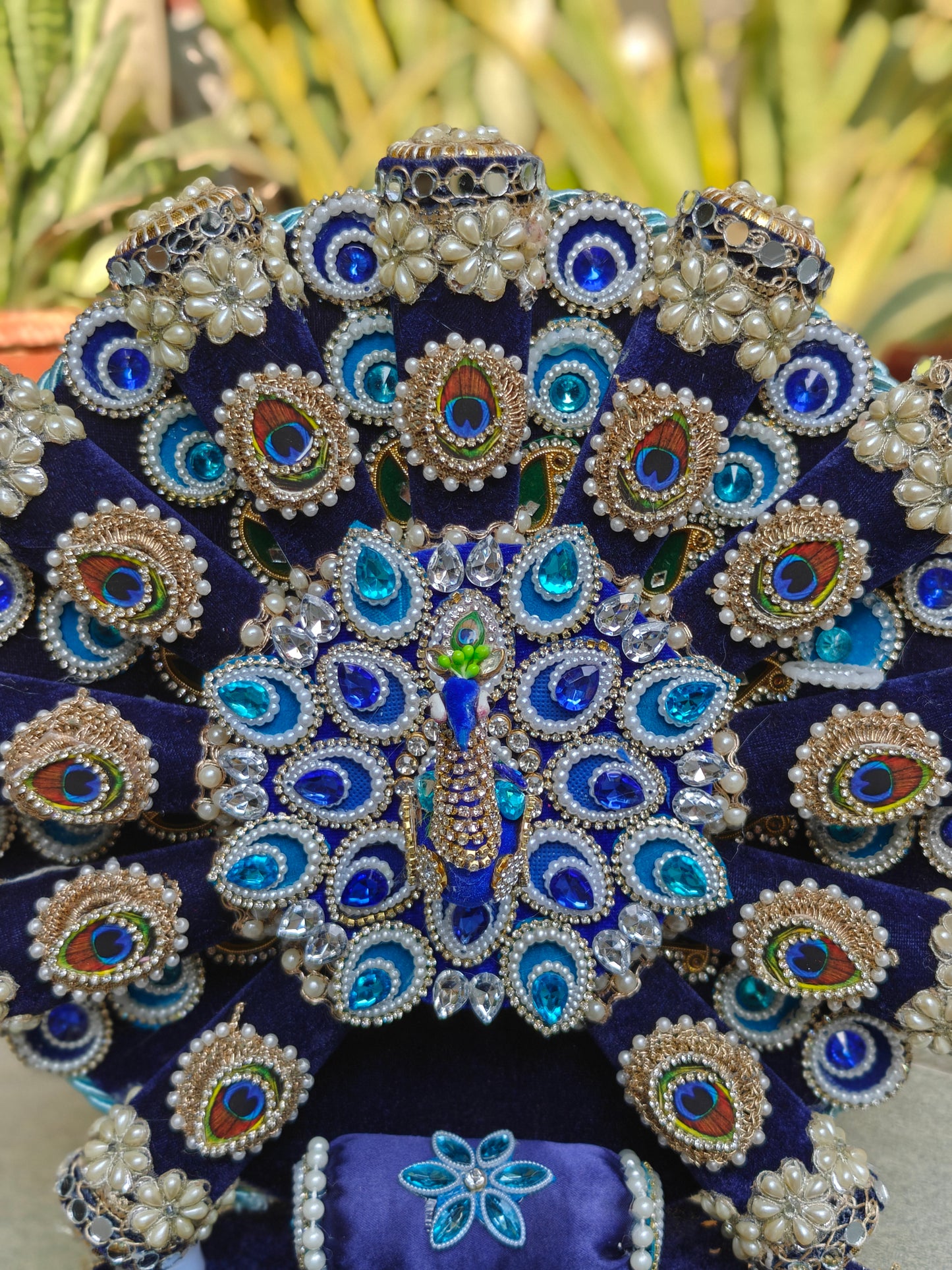 Close-up of handcrafted peacock singhasan backrest with real feather motifs, blue crystals, pearl detailing and zardozi embroidery on royal blue velvet