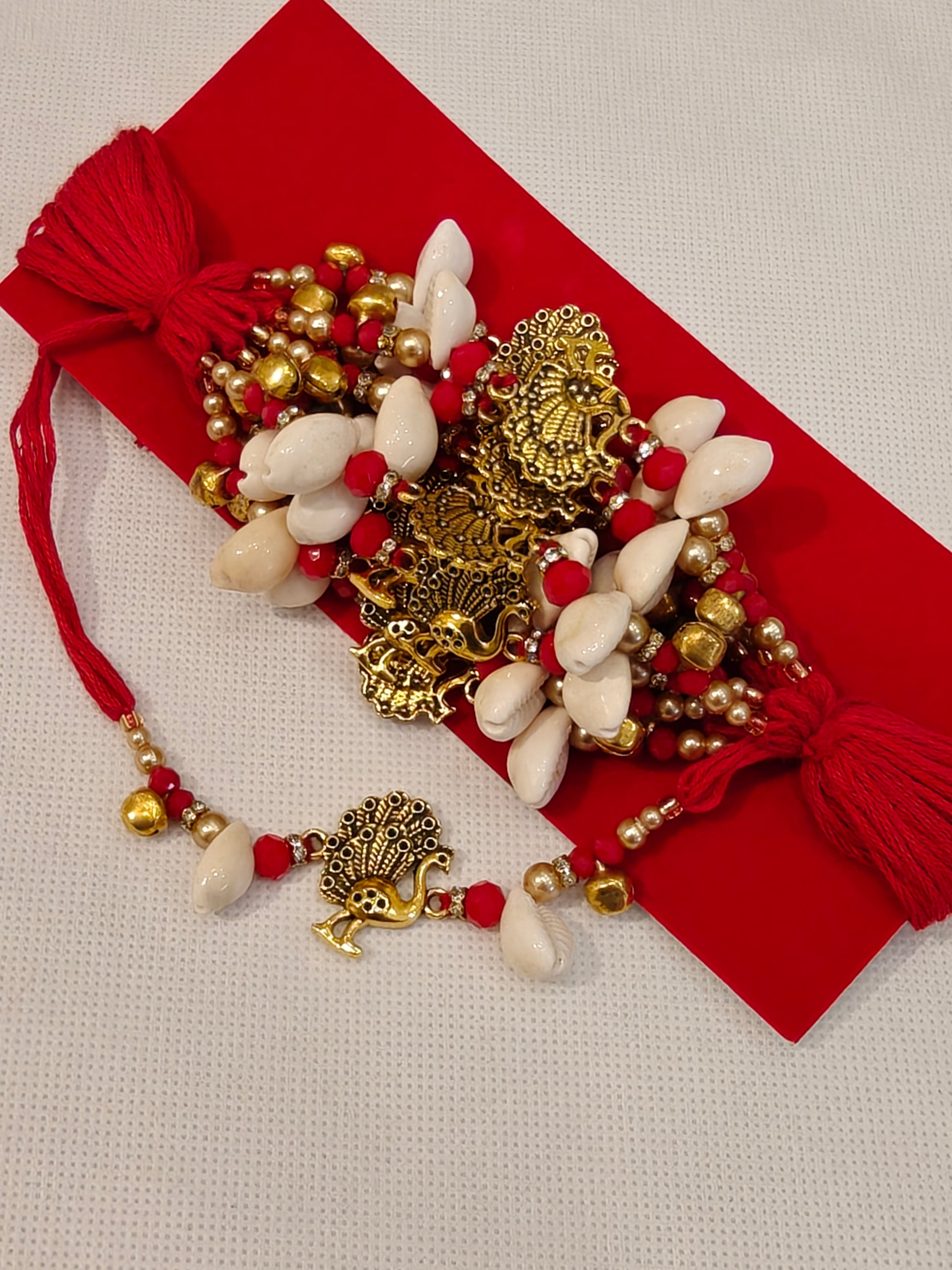 Handcrafted Hathlagi Kangan Dora with cowrie shells, red crystal beads, gold peacock charm and red tassels for Indian wedding rituals
