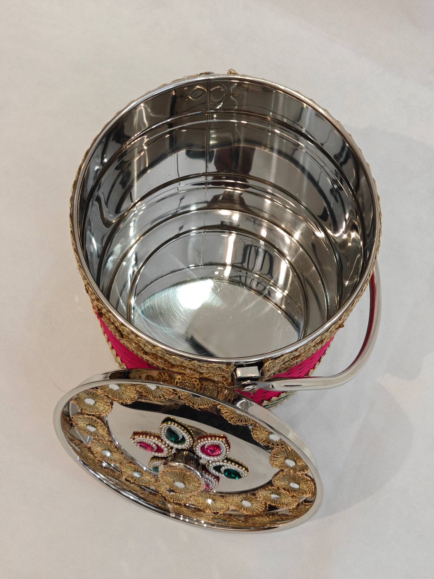 Open decorated stainless steel wedding bucket showing spacious mirror-finish interior, hinged lid with gold zardozi and kundan floral centre detail, and pink green brocade embellished body for Indian trousseau gifting