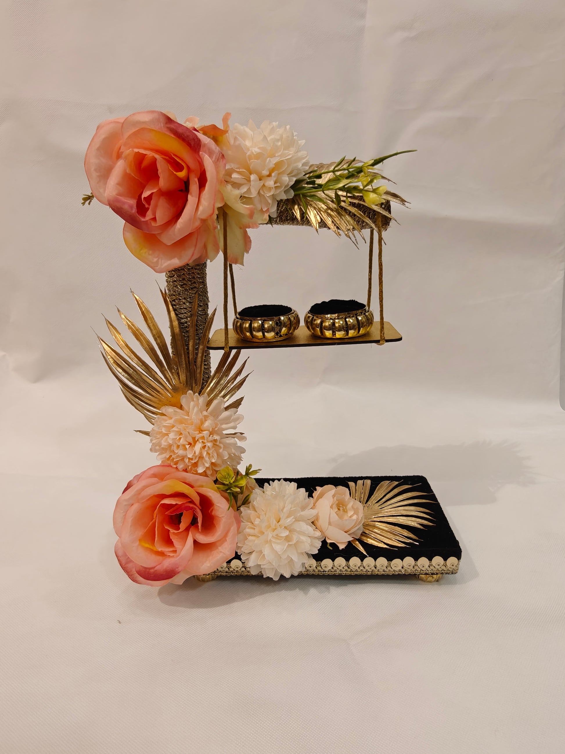 2-tier handcrafted wooden ring ceremony stand with peach and ivory silk flowers, gold palm leaves, jute-wrapped column, swing shelf, and two gold ring holders — by The Wedding Station