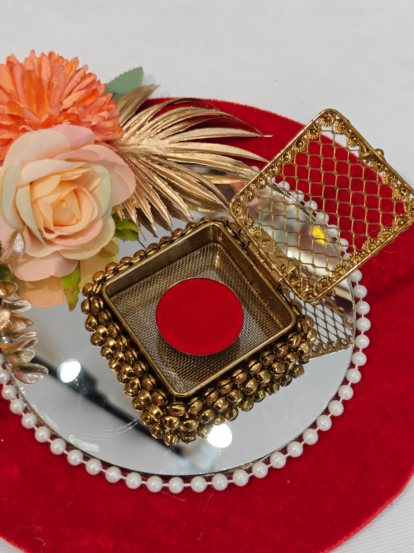 Decorative wedding coin platter with 9-inch red velvet MDF base, 
6-inch round mirror with pearl border, antique gold ghungroo coin 
box, and peach floral arrangement with golden dried leaves