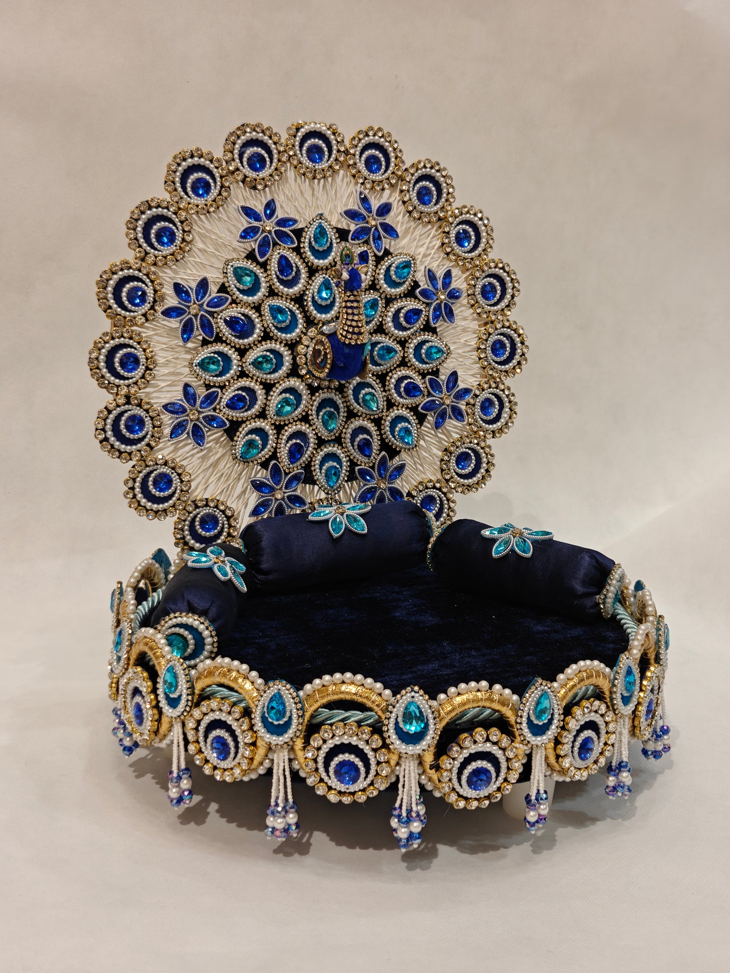 Handcrafted peacock singhaasan for Ladoo Gopal in royal blue and gold with gem embellishments, pearl beading, and detachable peacock feather backdrop — 12 inch MDF deity throne by The Wedding Station