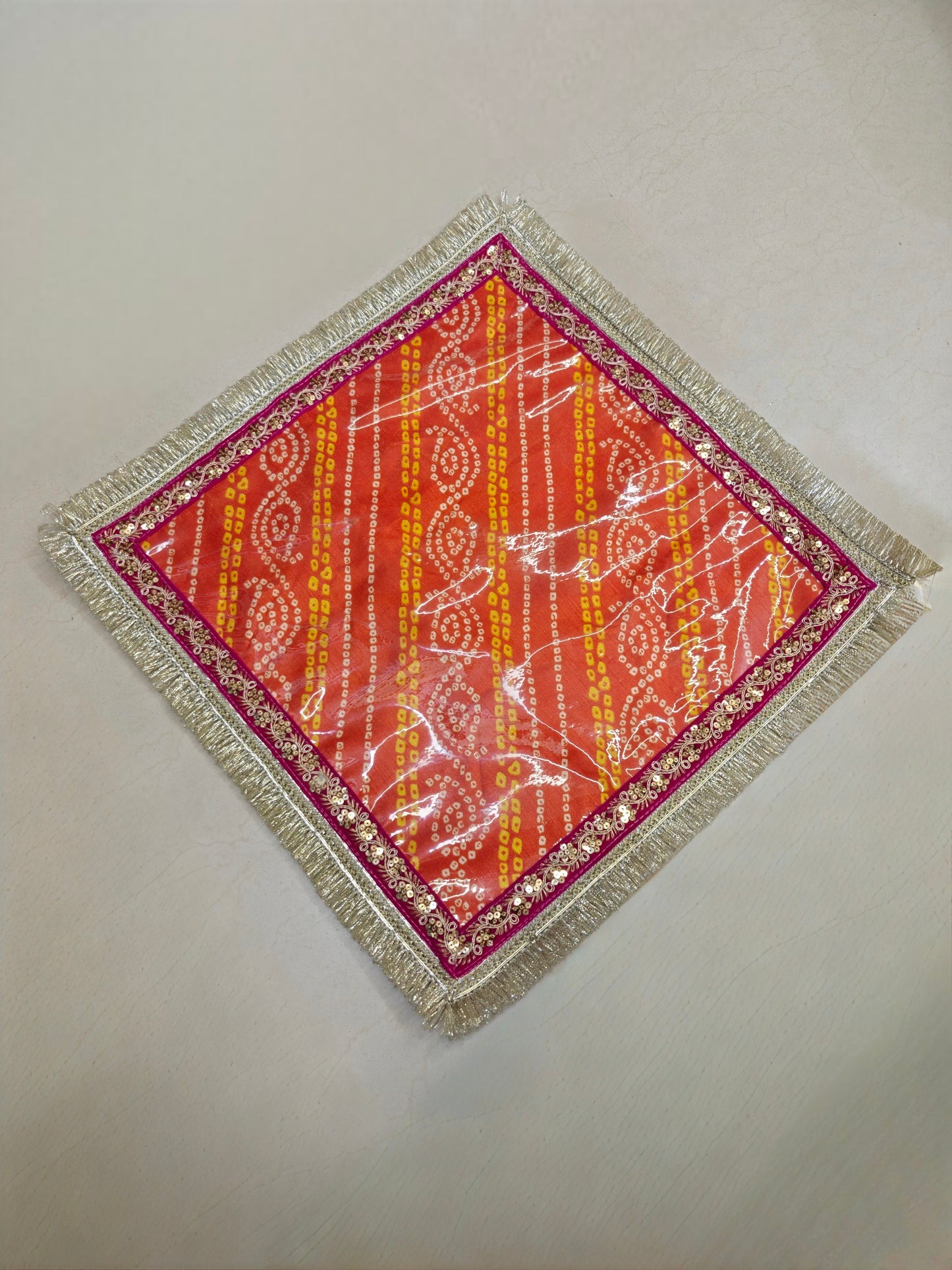 Orange and yellow Bandhani Dupion silk mangodi mat with transparent PVC sheet, magenta border, gold sequin lace and silver zari fringe, 20x20 inches, for Indian wedding rituals