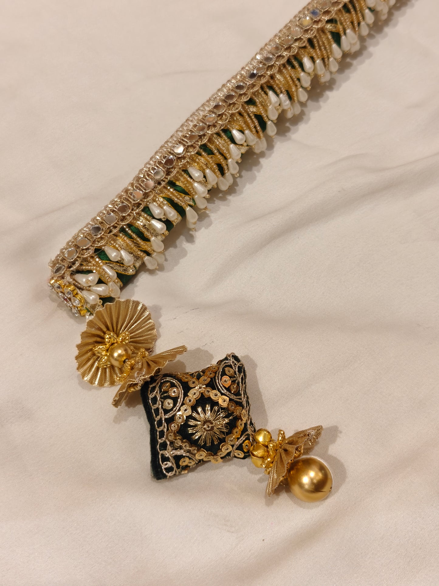 Close-up of dark green sarkanda tassel end with velvet cushion, zardozi embroidery, gold ghungroo and pearl fringe