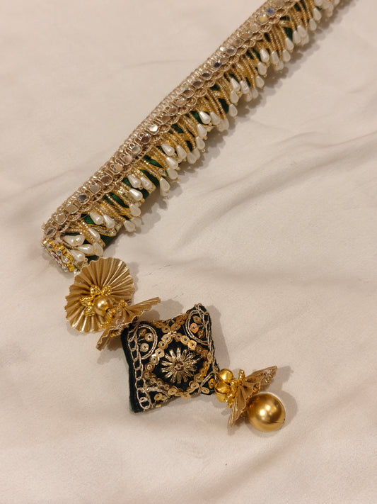 Close-up of dark green sarkanda tassel end with velvet cushion, zardozi embroidery, gold ghungroo and pearl fringe