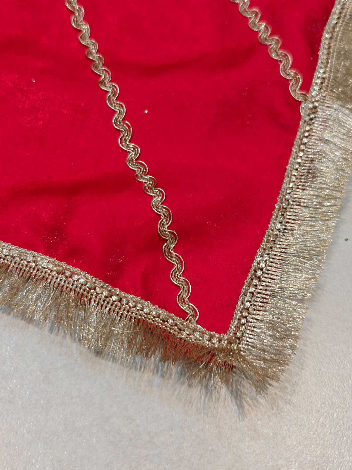 Close-up of a red thaal cover corner with golden zari wave lace, stone-studded border and golden fringe