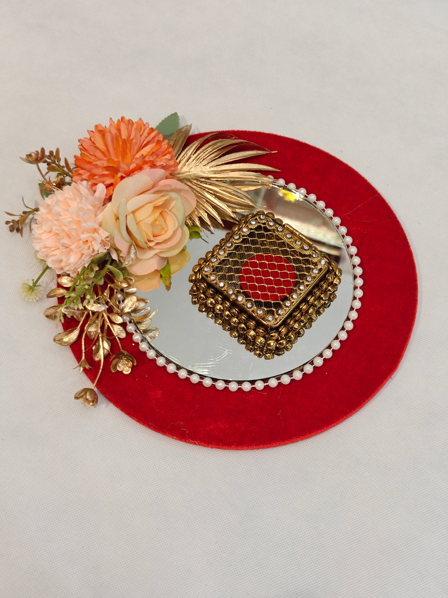 Decorative wedding coin platter with 9-inch red velvet MDF base, 
6-inch round mirror with pearl border, antique gold ghungroo coin 
box, and peach floral arrangement with golden dried leaves