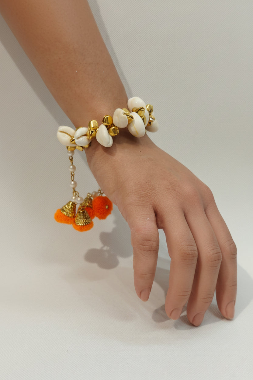 shell bracelet with gold accents, pearl chain danglers, and orange pom poms — Haldi and Mehendi jewellery by The Wedding Station