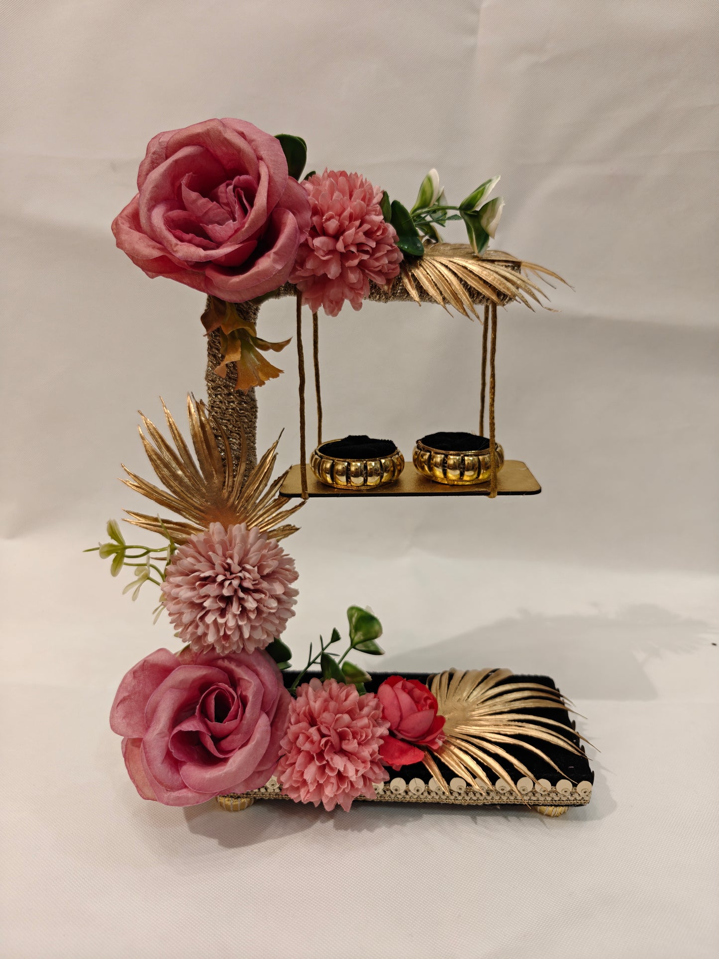 2-tier handcrafted wooden ring ceremony stand with dusty rose and mauve silk flowers, gold palm leaves, jute-wrapped column, swing shelf, and two gold ring holders — by The Wedding Station