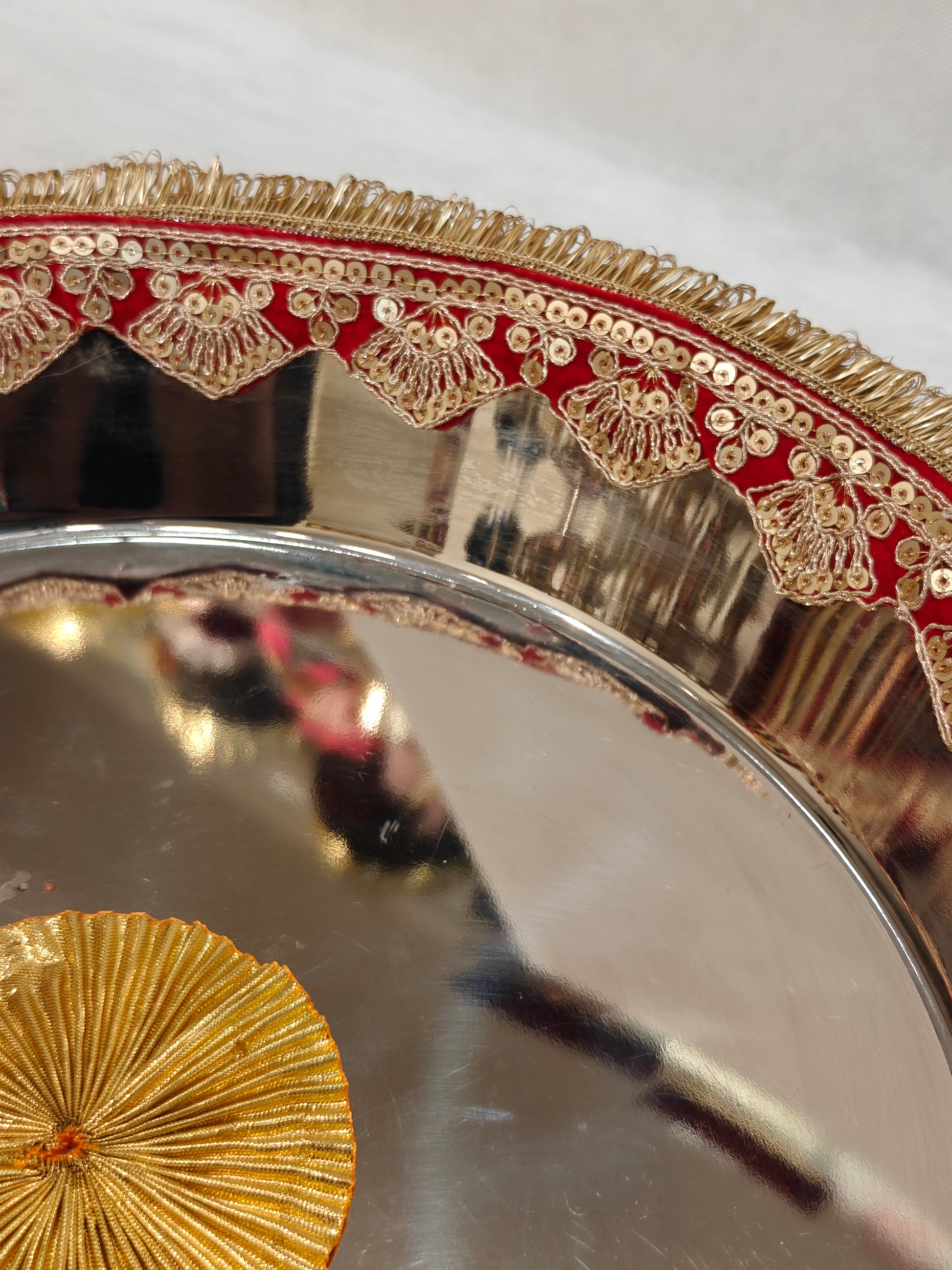 Close-up of red velvet and gold sequin embroidered scalloped border with zari fringe on decorated steel Pag Dhulai Thali for Indian wedding ceremony