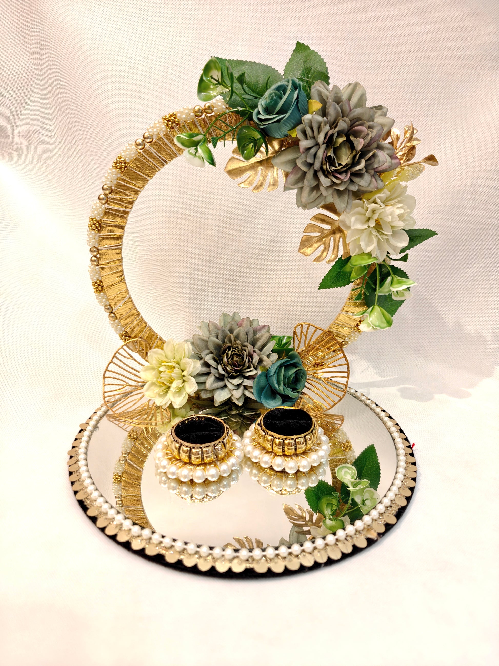Handcrafted ring ceremony platter with 11-inch mirror MDF base, gold crescent arch, sage green and grey silk flowers, teal roses, pearl-bordered tray, and pearl ring holders — by The Wedding Station