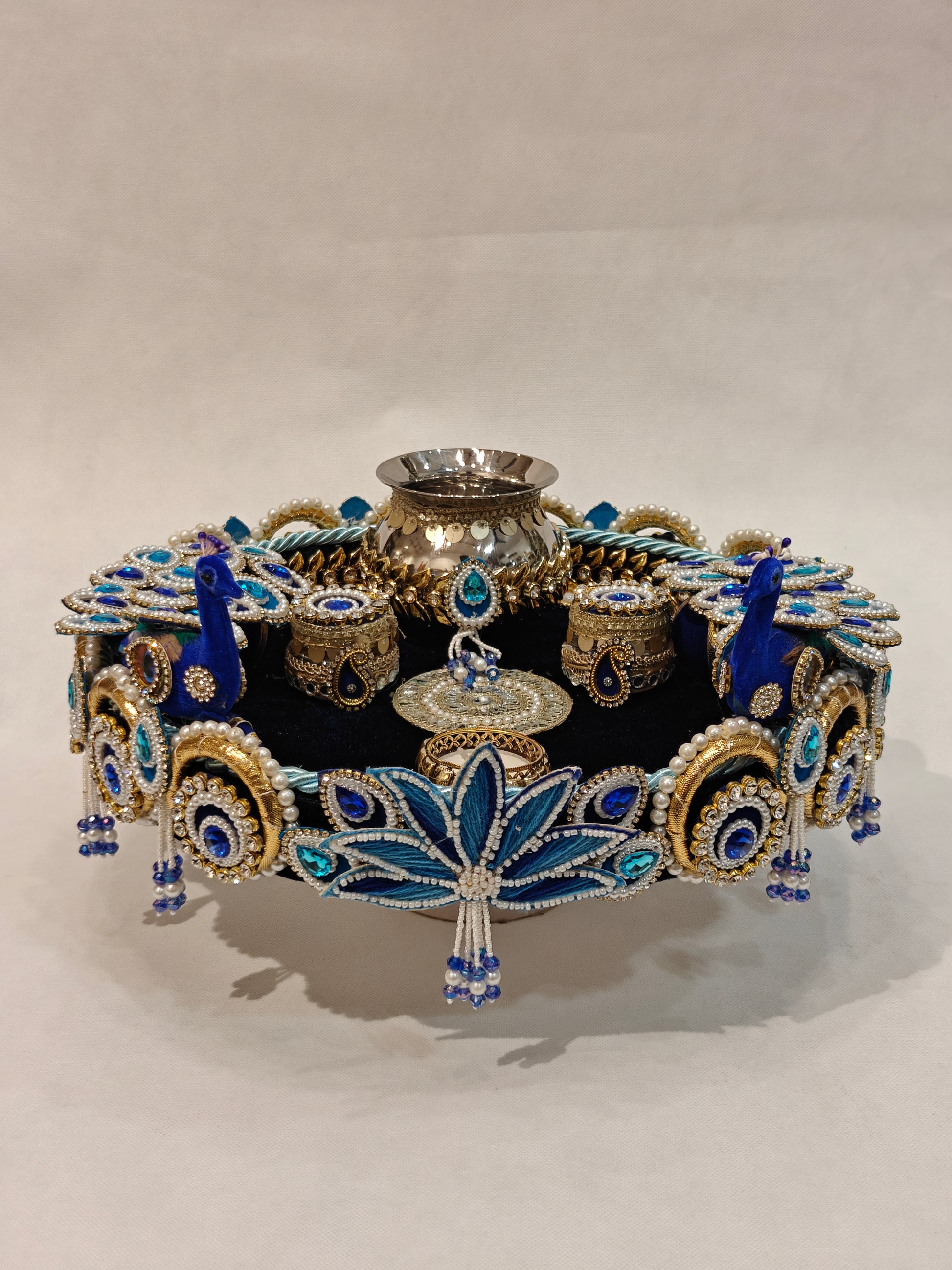 Handcrafted royal blue peacock pooja thali with pearl beadwork, gold zari, velvet base, silver kalash and lotus motif — bridal wedding puja thali by The Wedding Station