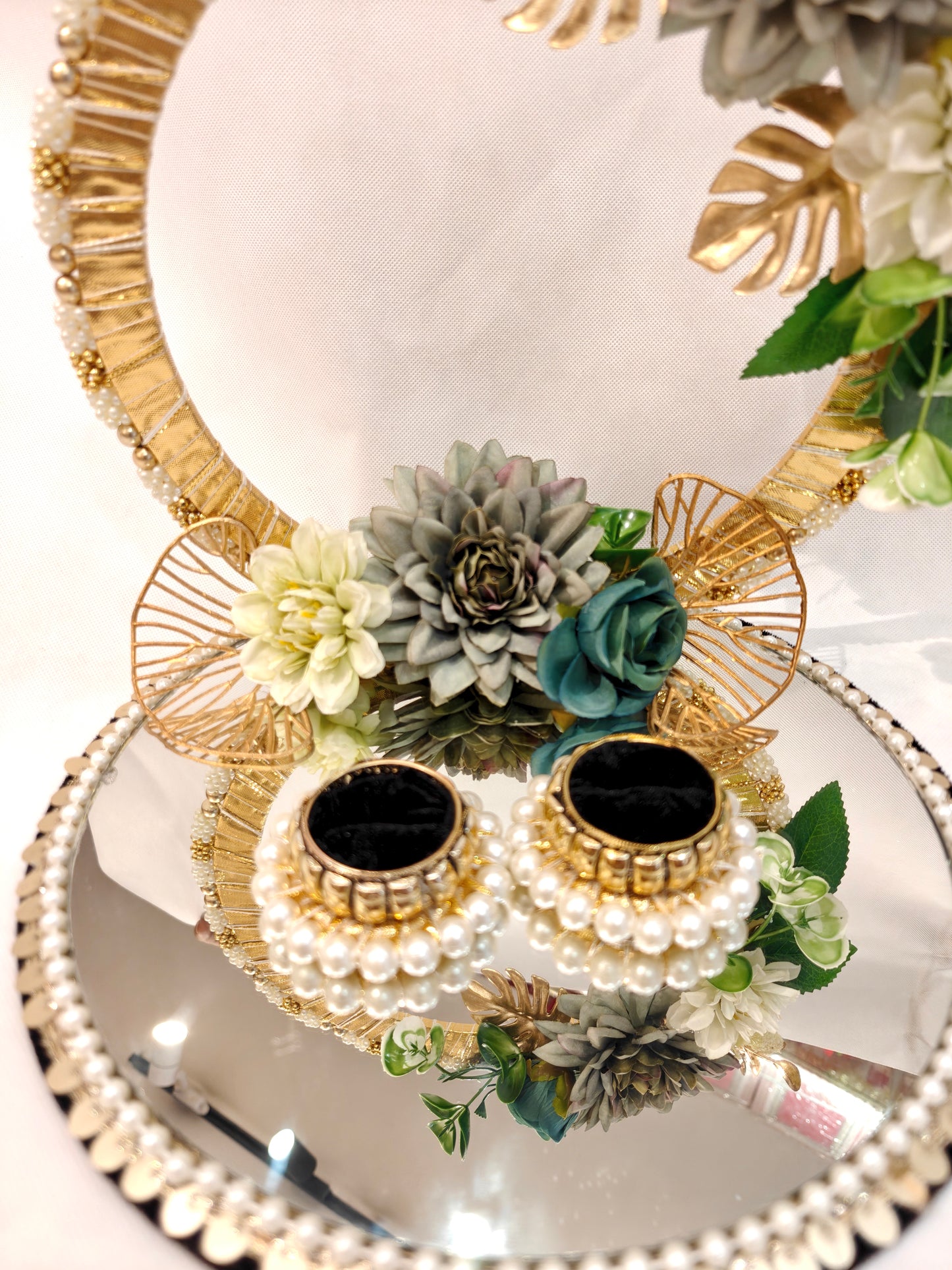Handcrafted ring ceremony platter with 11-inch mirror MDF base, gold crescent arch, sage green and grey silk flowers, teal roses, pearl-bordered tray, and pearl ring holders — by The Wedding Station