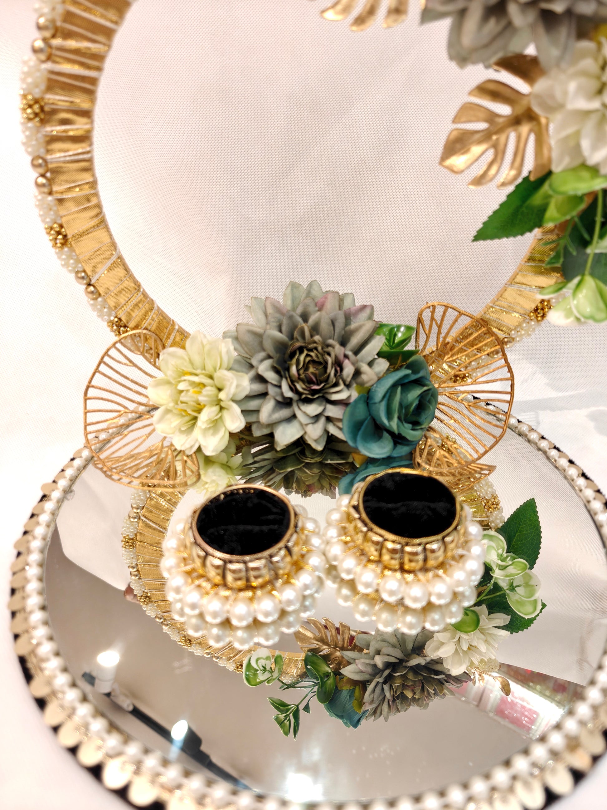 Handcrafted ring ceremony platter with 11-inch mirror MDF base, gold crescent arch, sage green and grey silk flowers, teal roses, pearl-bordered tray, and pearl ring holders — by The Wedding Station