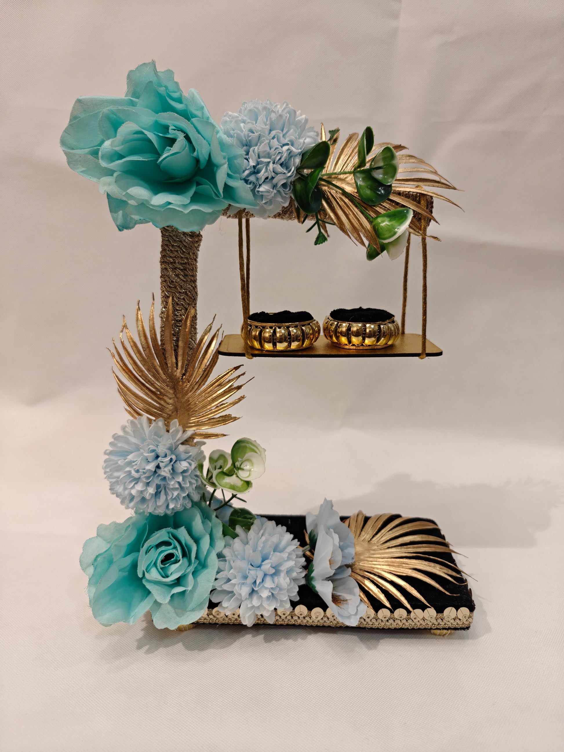 2-tier handcrafted wooden ring ceremony stand with teal and baby blue silk flowers, gold palm leaves, jute-wrapped column, swing shelf, and two gold ring holders — by The Wedding Station