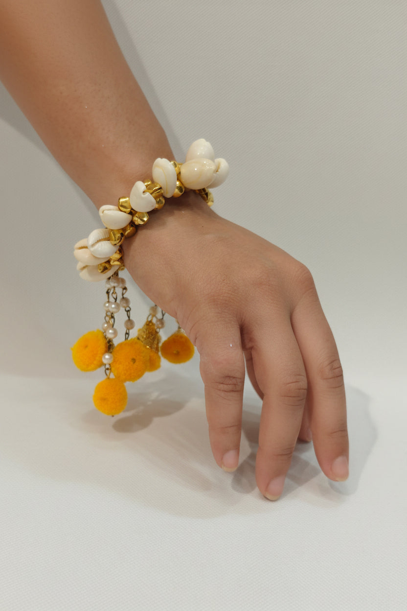 shell bracelet with gold accents, pearl chain danglers, and yellow pom poms — Haldi and Mehendi jewellery by The Wedding Station