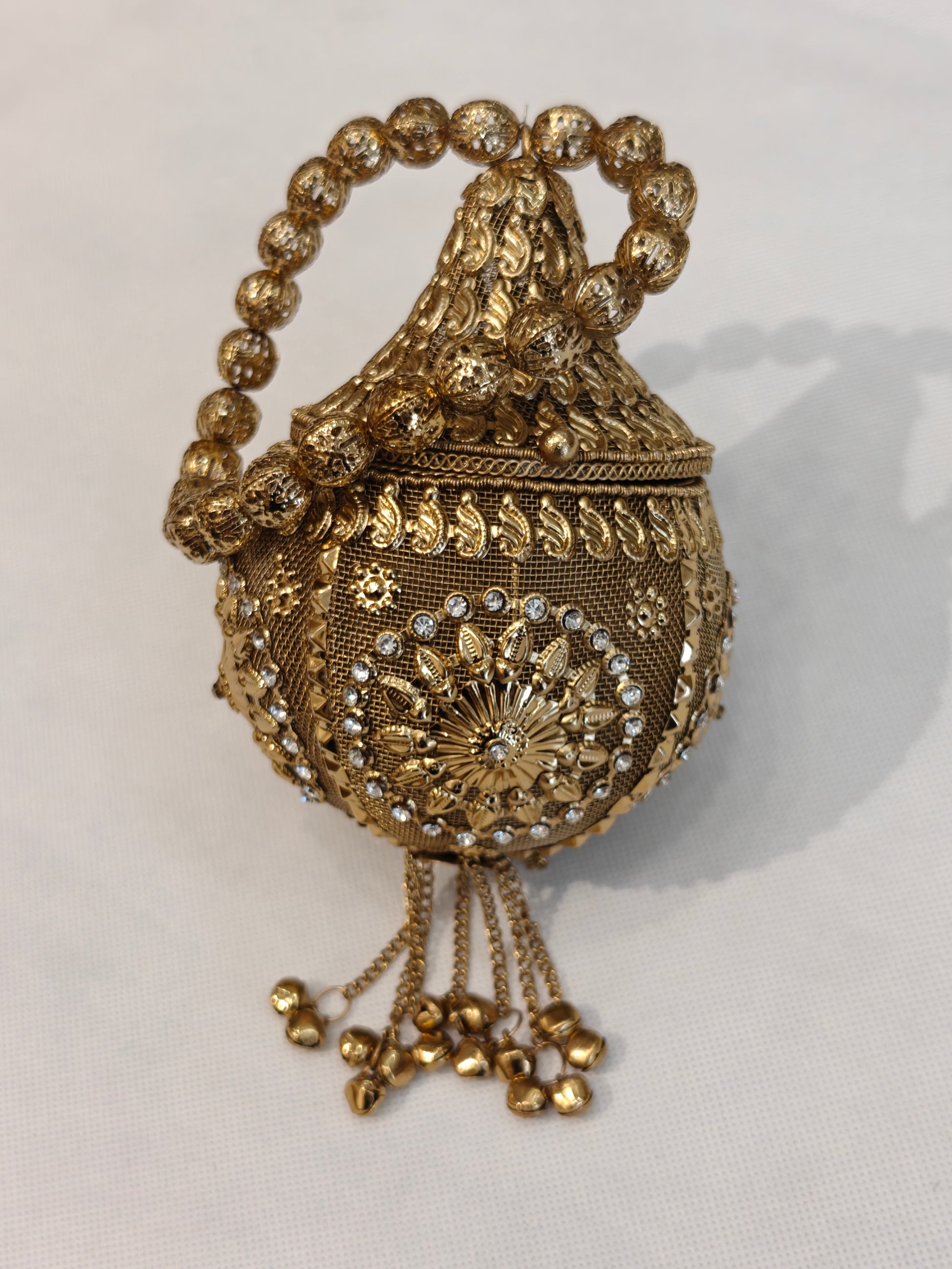 Handcrafted gold brass mesh round potli bag with crystal rhinestones, raised paisley motifs, floral sunburst medallion, ghungroo bell chain tassels and filigree bead loop handle — bridal wedding potli by The Wedding Station Meerut