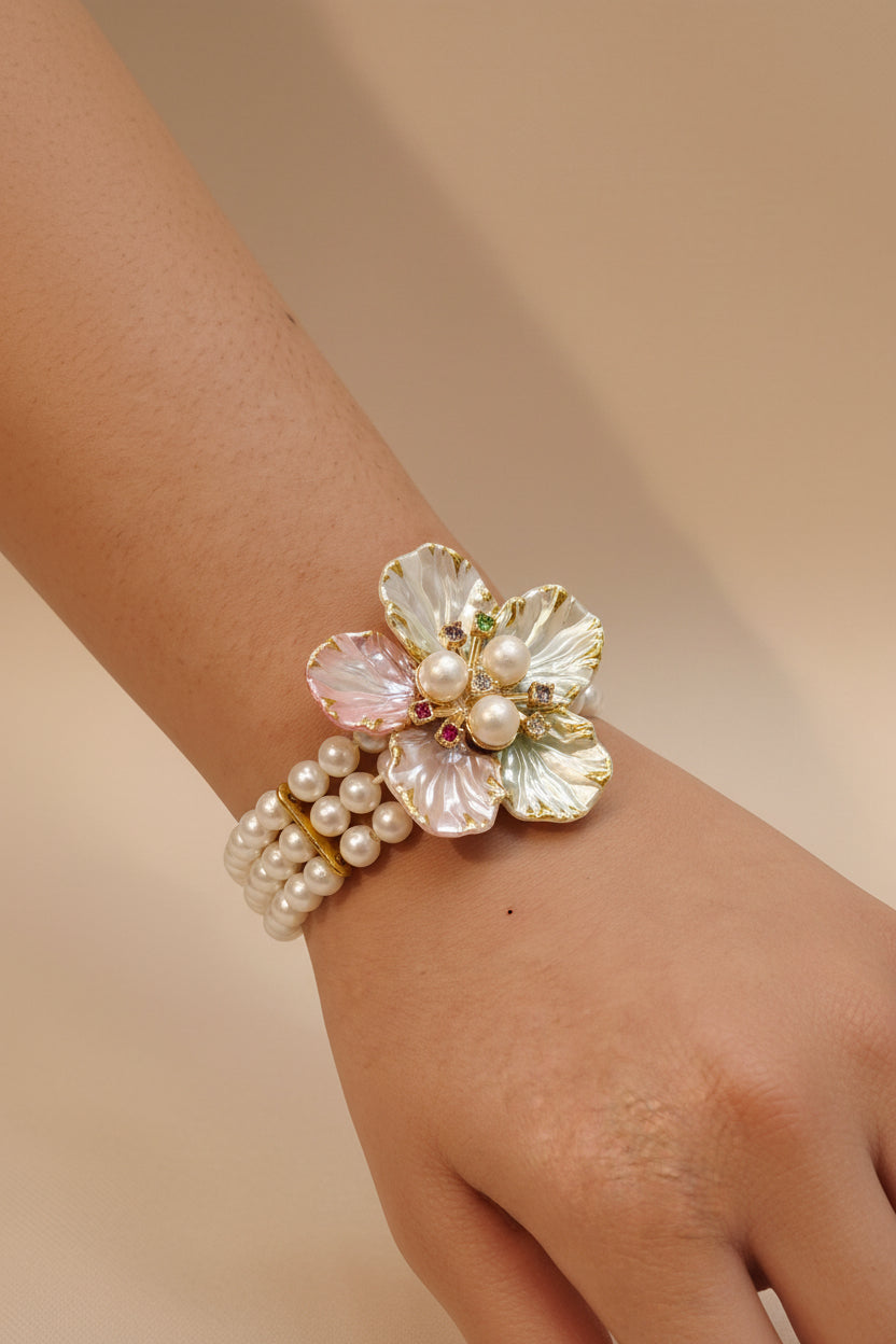 Floral pearl bracelet with pastel enamel petals in pink, white, and champagne, pearl centres, crystal accents, and triple-strand pearl band — bridal jewellery by The Wedding Station