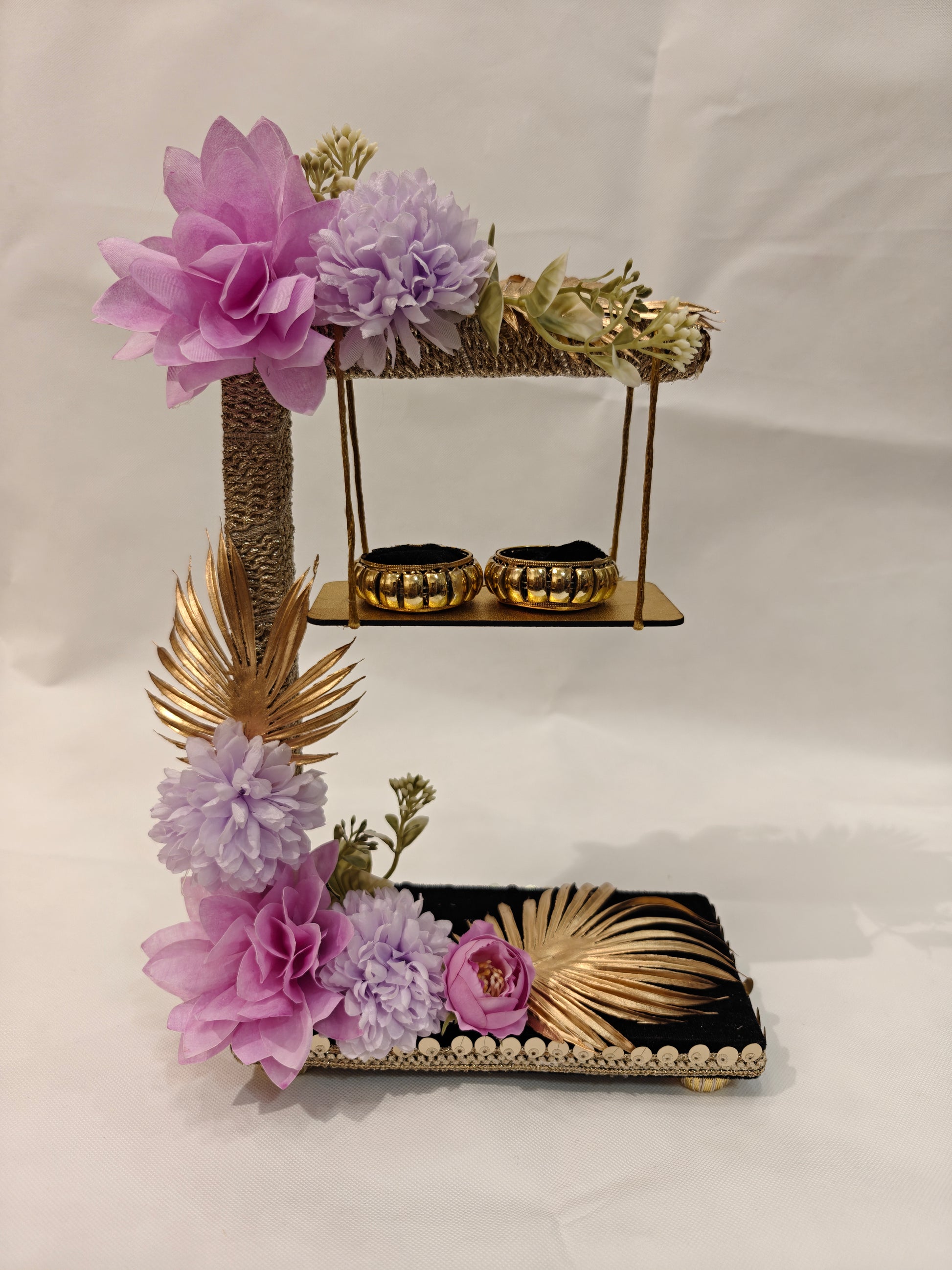2-tier handcrafted wooden ring ceremony stand with lavender and lilac silk flowers, gold palm leaves, jute-wrapped column, swing shelf, and two gold ring holders — by The Wedding Station
